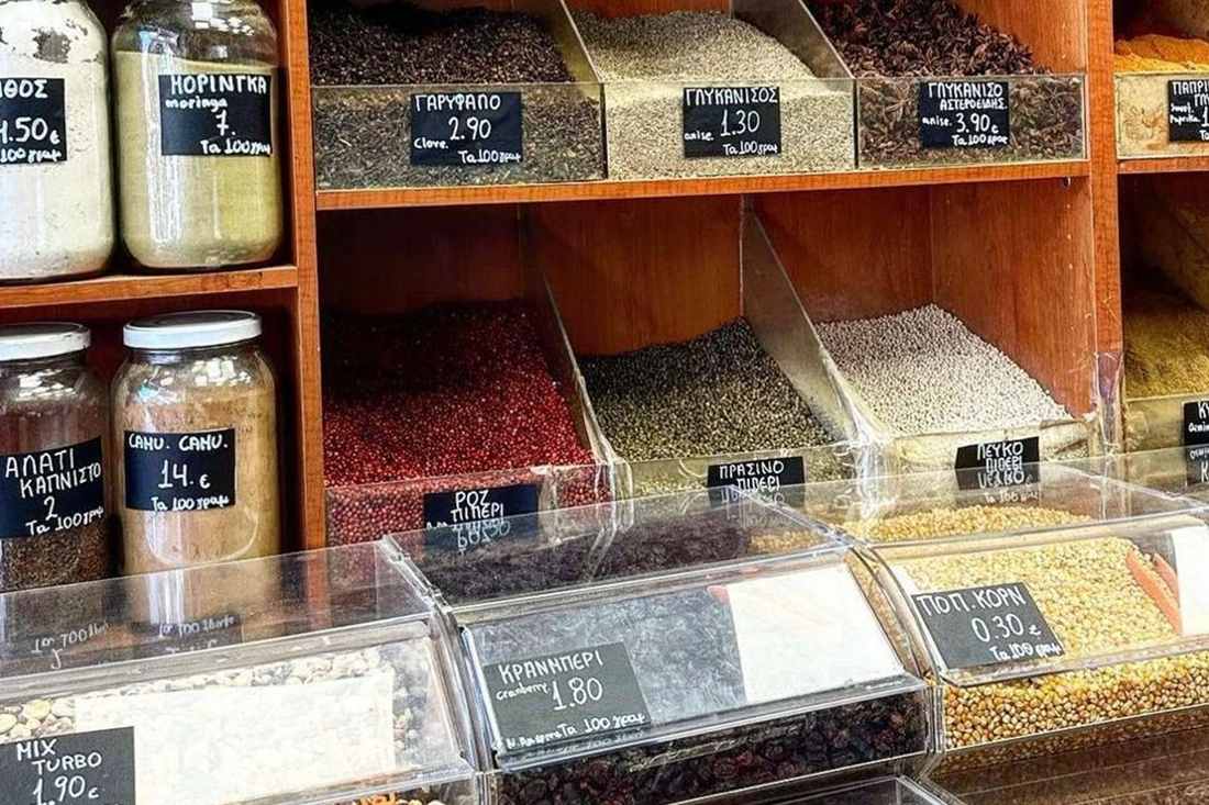 Shelves and bins of spices and dried berries with black chalk labels for clove, anise, pink pepper, cranberry and popcorn in a spice shop