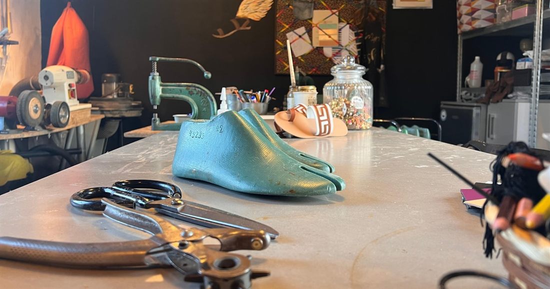 A leather workbench with scissors, a green shoe last, sandal straps and tools laid out at an Athens sandal workshop.
