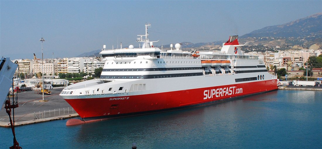 A red and white Superfast ferry moored at the port of Patras with the city and hills behind