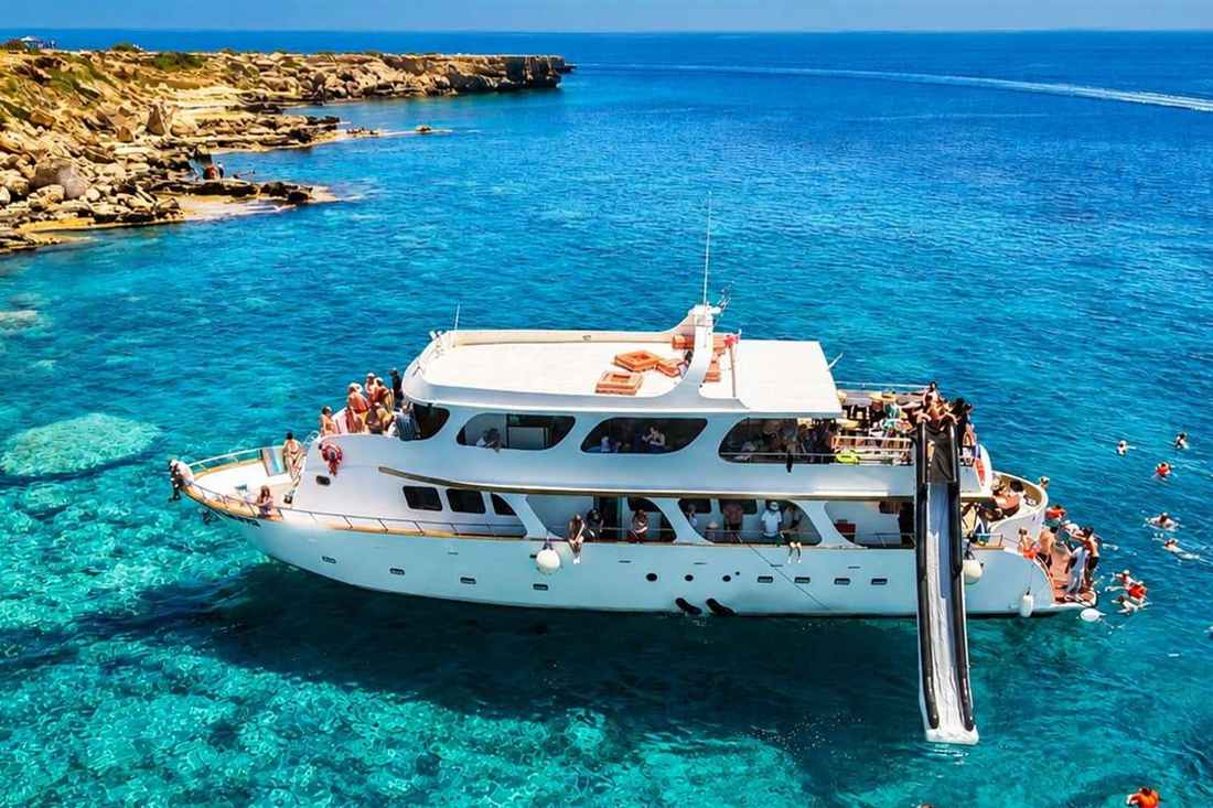 A white cruise yacht with a water slide anchored in the turquoise Blue Lagoon near Cape Greco as guests swim