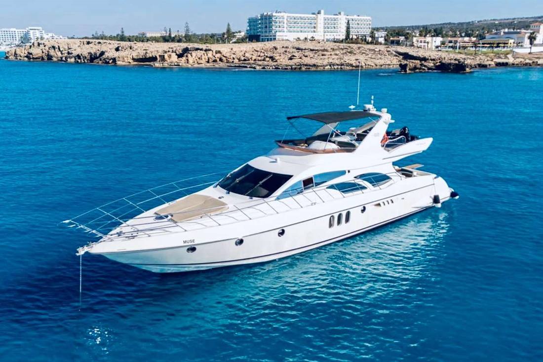 White motor yacht at anchor on deep blue water off a rocky headland with white hotel buildings behind