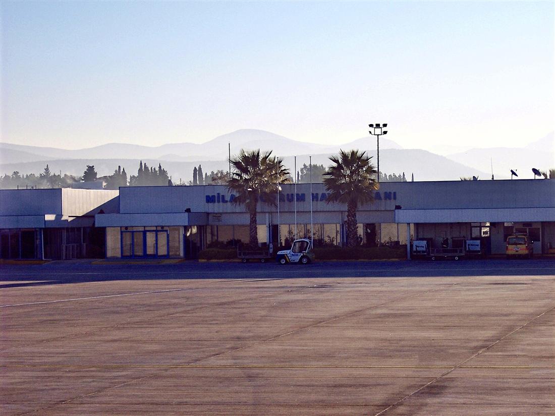 The terminal building of Milas–Bodrum Airport seen from the apron, with palm trees in front.