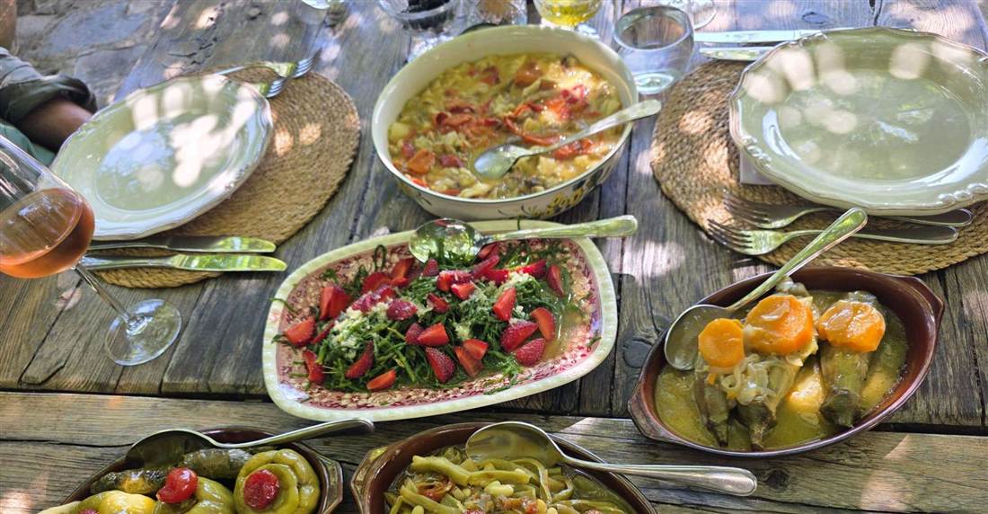 Home-cooked Turkish dishes on a wooden table: a tomato salad, stuffed peppers and a bowl of stew.