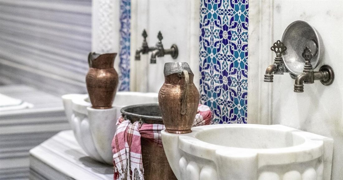 Marble wash basins with copper bowls and blue tiles inside a Bodrum hamam.