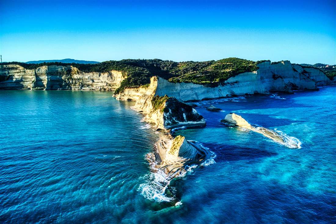 The white cliffs and sea caves of Cape Drastis rising from blue water on the north-west coast, a stop on a Corfu cave tour.