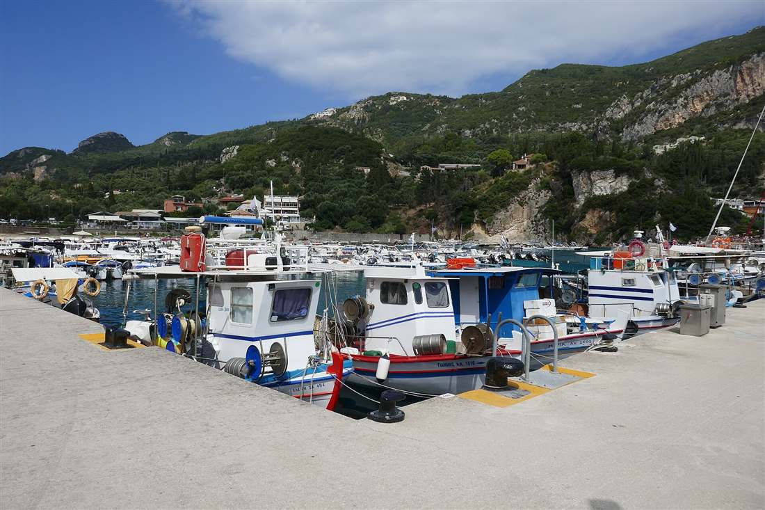 Fishing and tour boats moored in the harbour at Paleokastritsa below green hills, Corfu.
