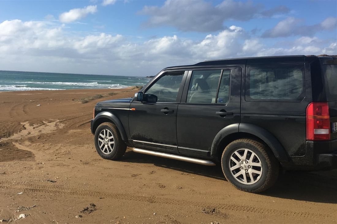 A dark Land Rover parked on a sandy beach track beside the sea on a Corfu jeep safari.