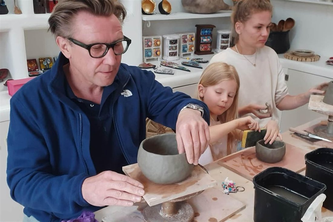 A man and a girl shaping clay bowls at pottery wheels in a studio during a Corfu pottery class.