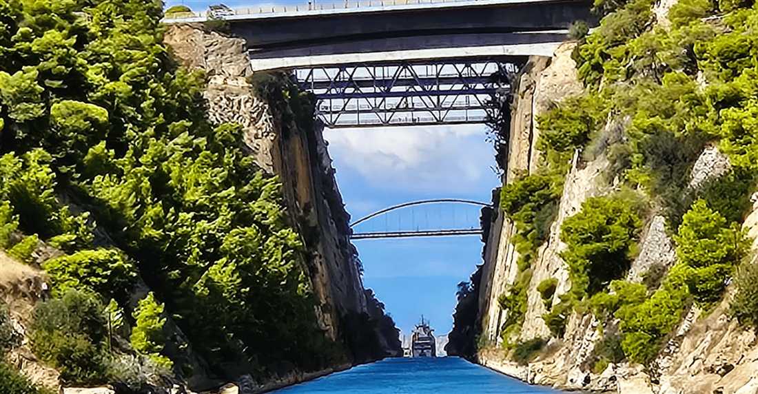 Road and rail bridges span the Corinth Canal between steep green walls, with a ship far down the channel