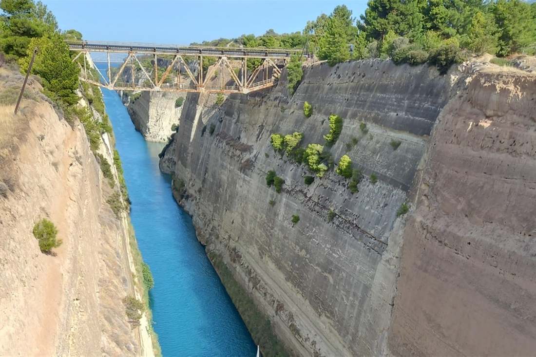 The Corinth Canal, a narrow channel of blue water between steep sandstone walls, crossed by a bridge.