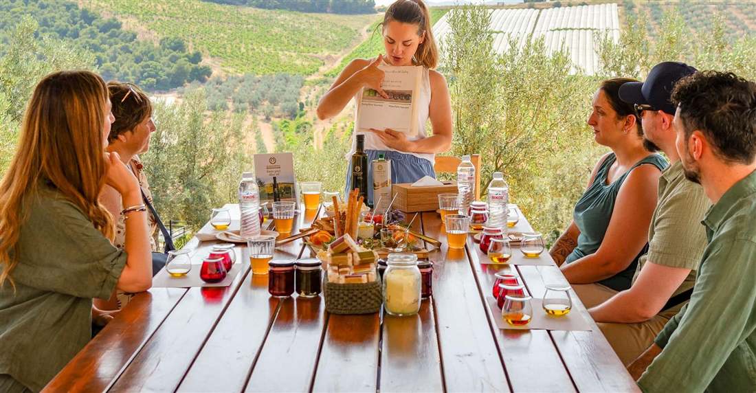 Guests at a long table tasting olive oils and local products in an olive grove near Corinth