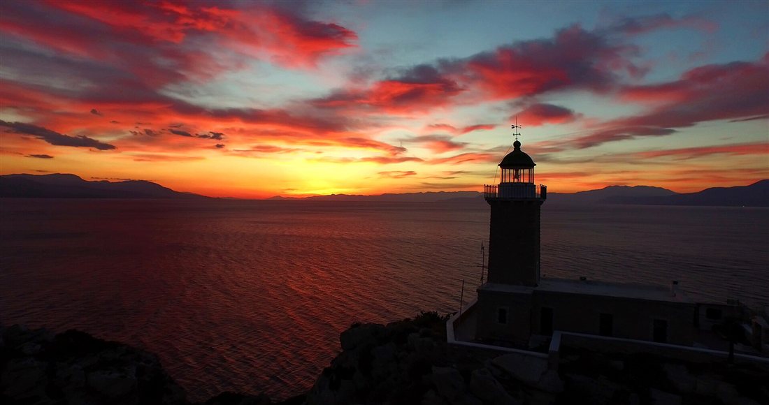 The Melagavi lighthouse on Cape Perachora against a red and orange sunset over the Gulf of Corinth