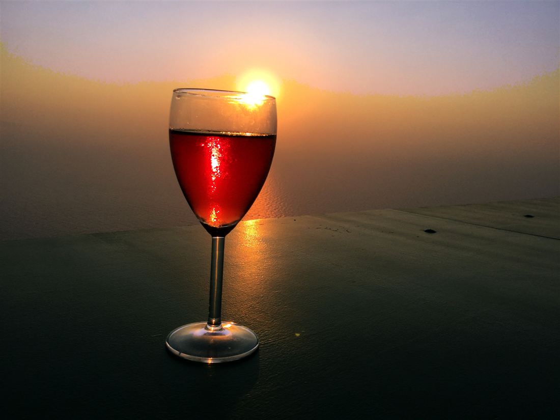 A glass of red wine glowing in the evening sun on a winery terrace above the sea, the moment a Corinth wine tasting is built around.