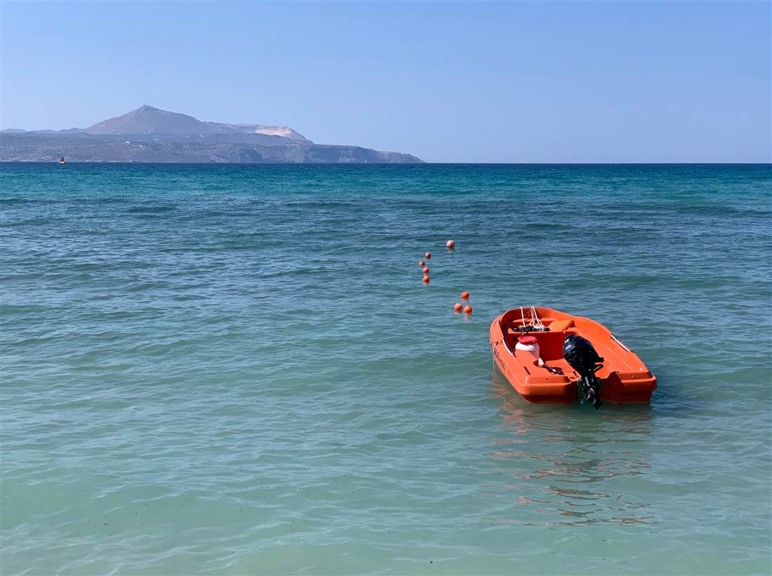 An orange licence-free motorboat moored in the turquoise water of Almyrida bay, the kind of boat hired for Crete boat rental.