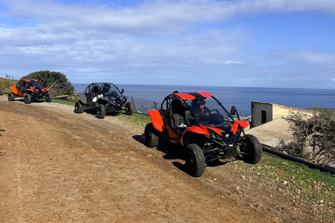 A convoy of off-road buggies on a dirt track above the sea in Crete, under a blue sky.
