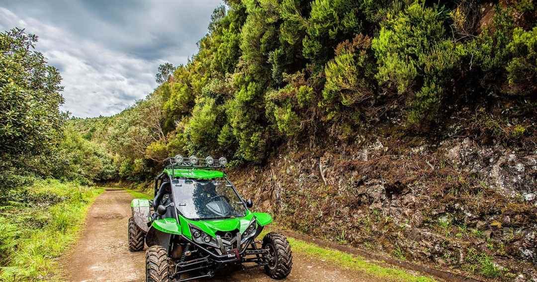 A green off-road buggy on a dirt track through dense green forest in the Cretan hills.