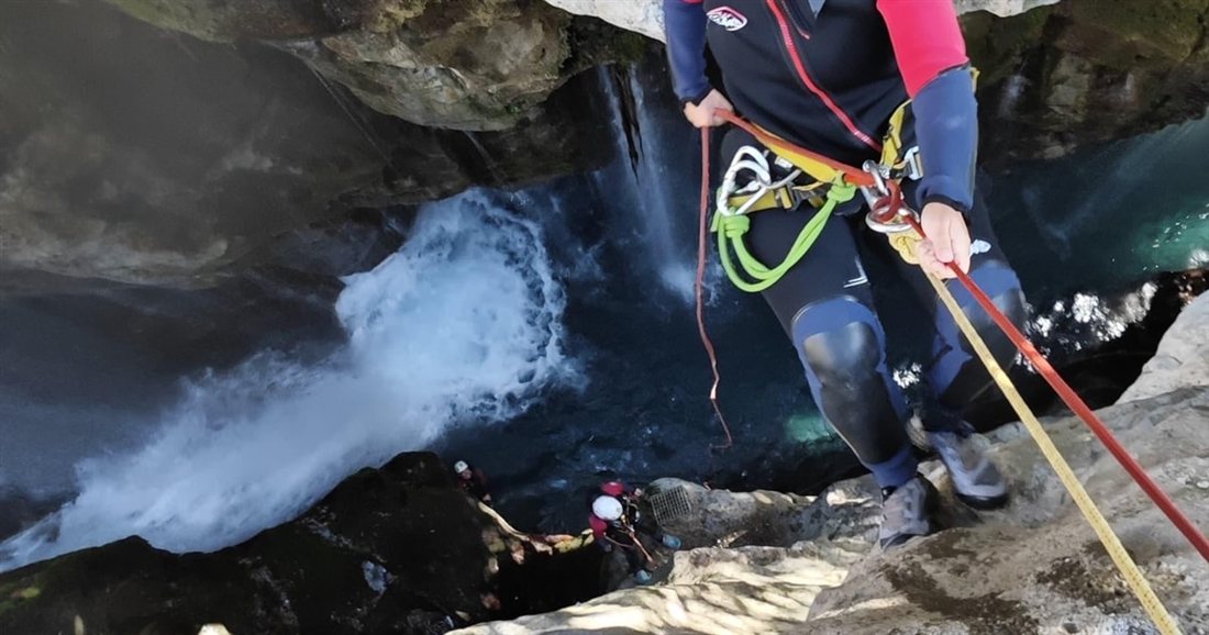 A canyoner in a harness rappelling down a rope beside a waterfall during Crete canyoning in the Kourtaliotiko Gorge.