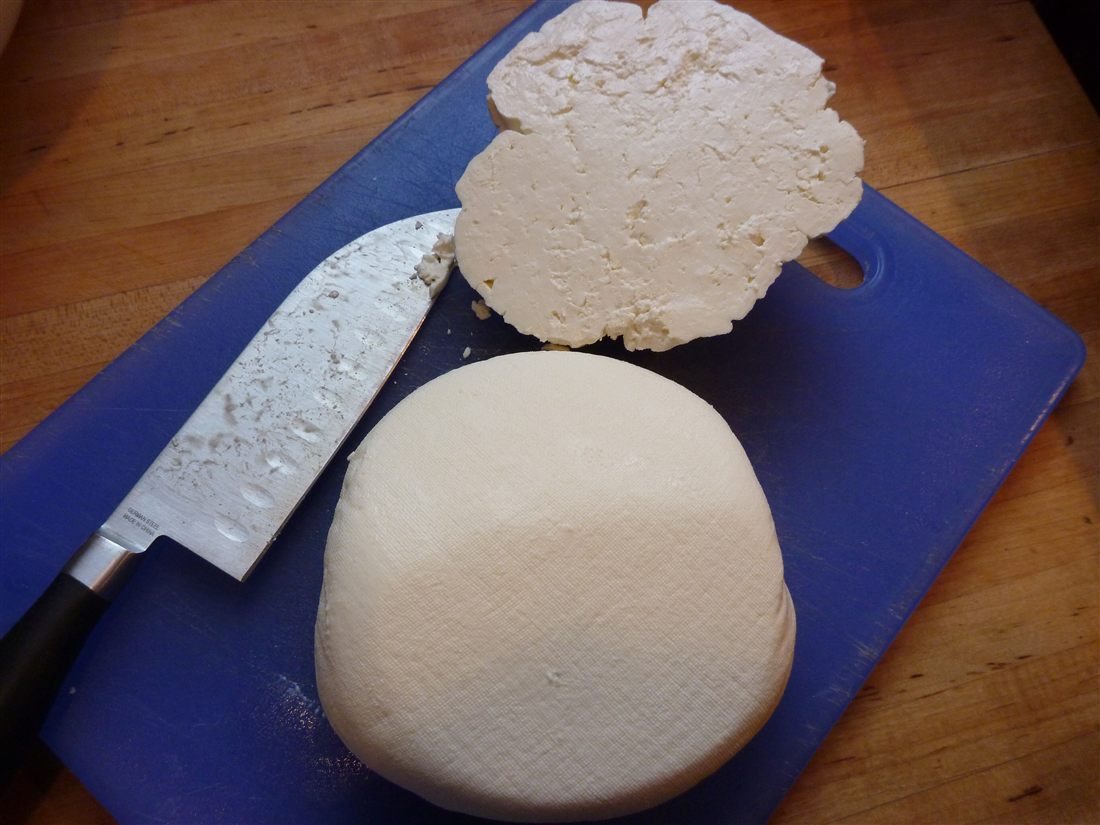 A round of fresh white myzithra cheese cut on a board, one of the cheeses served at a Crete cheese tasting.