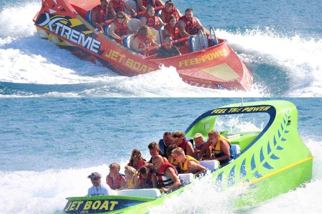 Two jet boats full of passengers race across the sea in clouds of white spray, a red one above and a green one below, on a Crete jet boat ride.