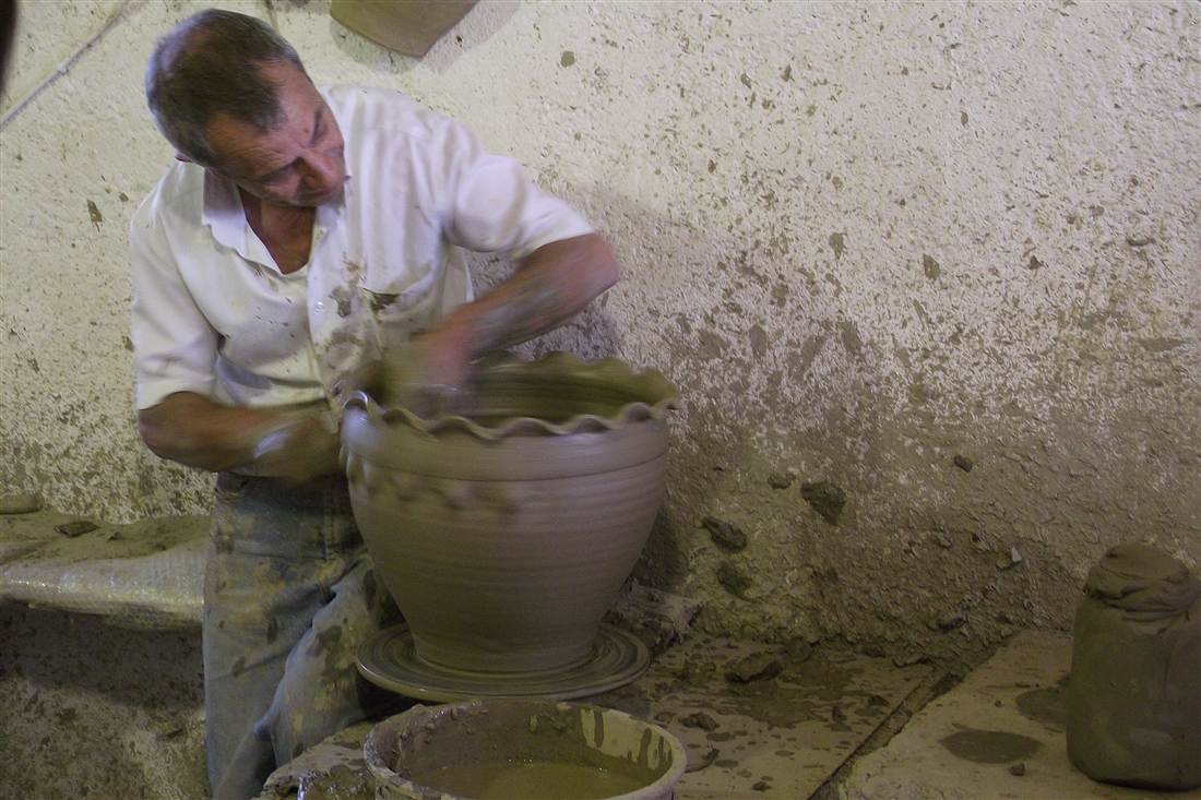 A potter shaping a large clay pot on the wheel in a Thrapsano workshop, the craft taught in a Crete pottery class.