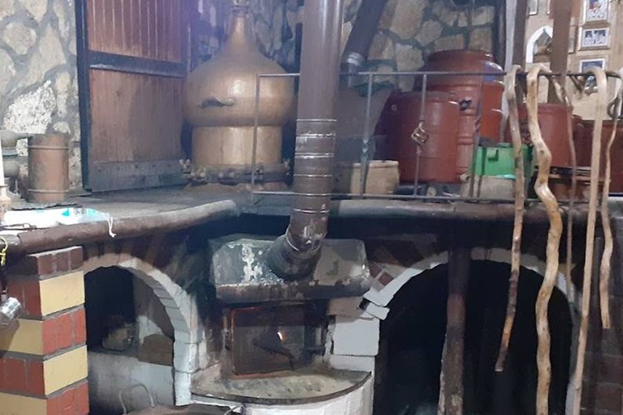 A Cretan raki distillery with a copper still, clay jars and a wood-fired brick hearth.