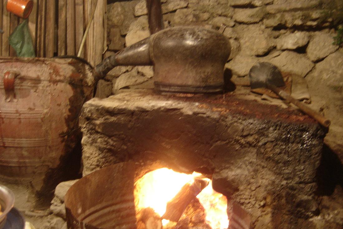 A copper raki still on a stone hearth in Crete, with a wood fire burning below the kettle.