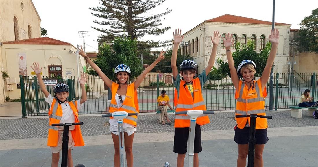 A family in helmets and orange vests waving from their segways in the old town of Rethymno on a Crete segway tour.