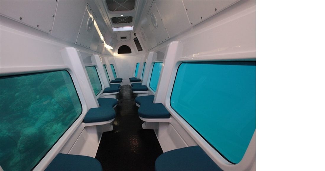 The underwater cabin of a semi-submarine, with rows of blue seats facing large windows that look into green sea water, on a Crete submarine trip.