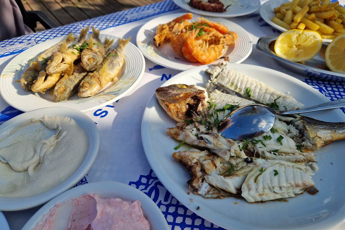Table of Cypriot fish meze with fried small fish, prawns, a grilled sea bream, chips with lemon and two creamy dips on a blue and white cloth