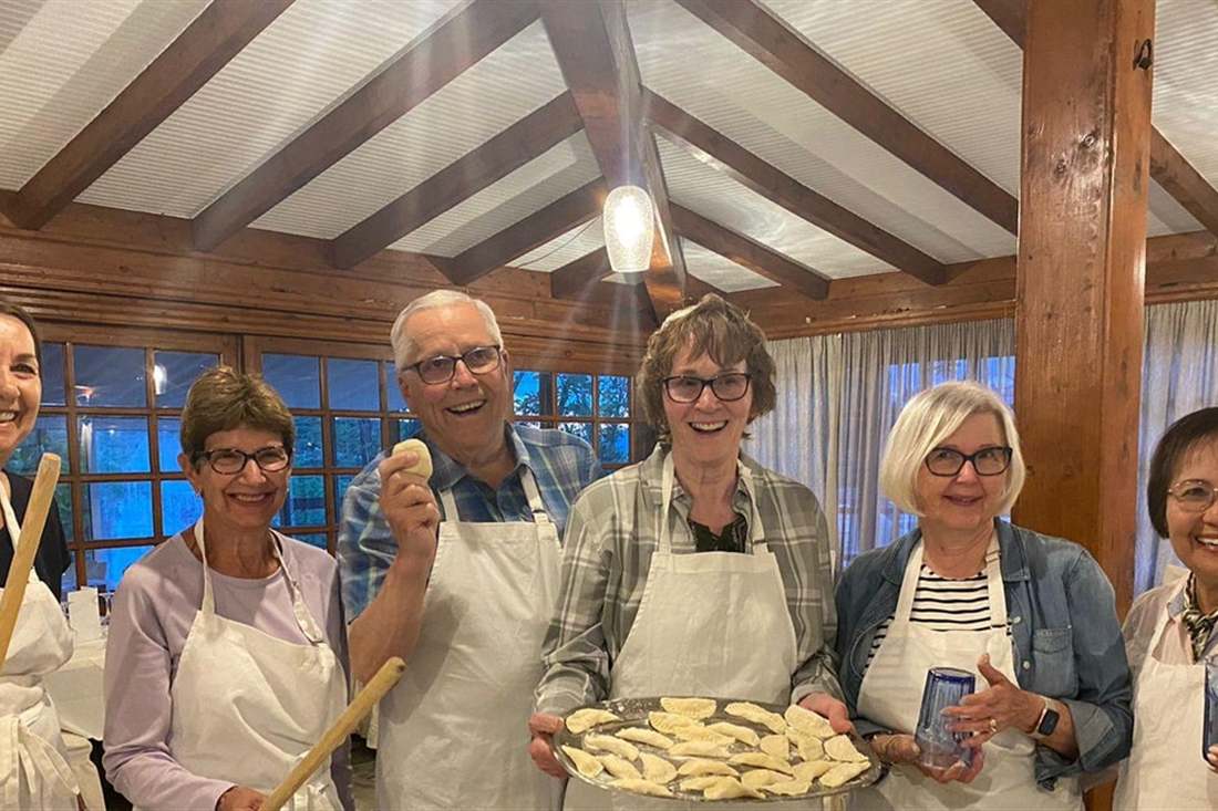 Guests in aprons holding rolling pins and a tray of handmade pies at a Delphi cooking class.