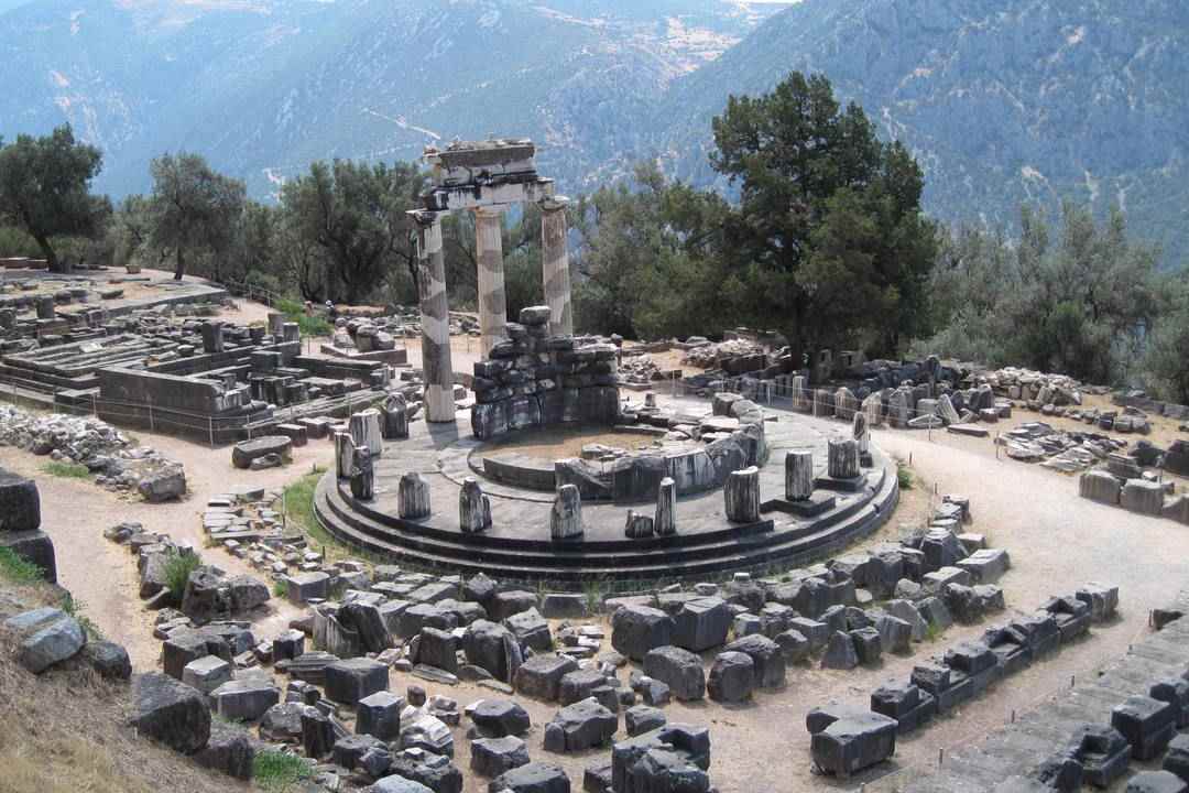 The round Tholos of Athena Pronaia at Delphi, with its three standing columns, among stone ruins below Mount Parnassus.