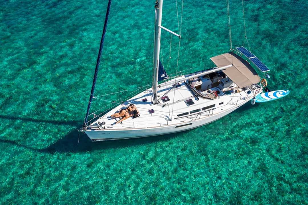 A white sailing yacht at anchor in clear green-blue water off Dia island, seen from above.