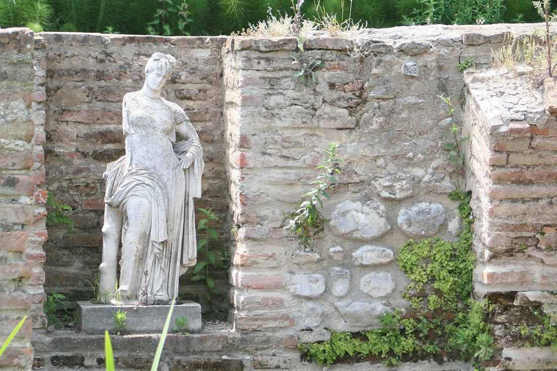 A marble statue of a draped woman standing in a brick niche on a stone base at the Dion archaeological site