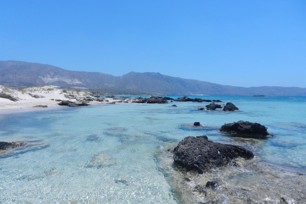Clear shallow water, dark rocks and white dunes at Elafonisi, waded on an Elafonisi day trip from Heraklion