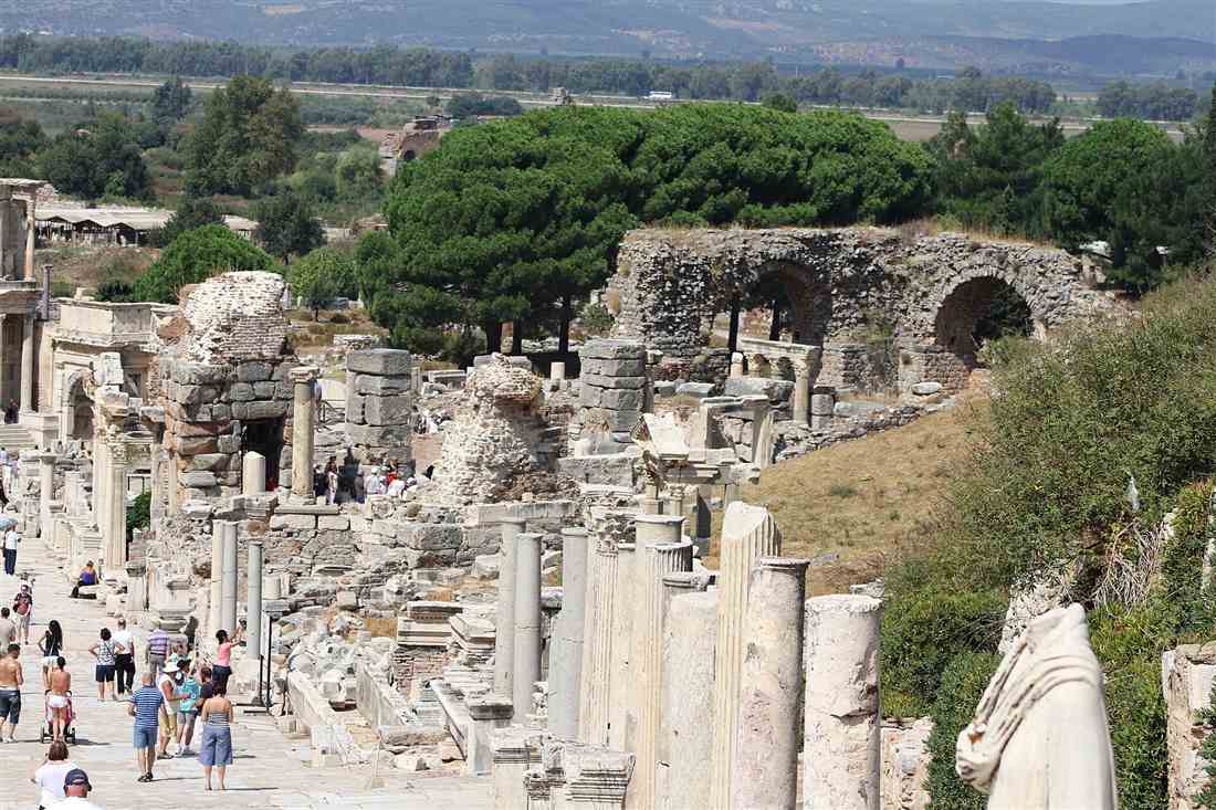 Curetes Street at Ephesus lined with marble columns and ruins, with visitors walking down the slope.
