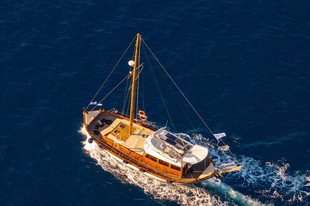 A traditional wooden sailing boat with one mast and a white wake, seen from above on deep blue sea