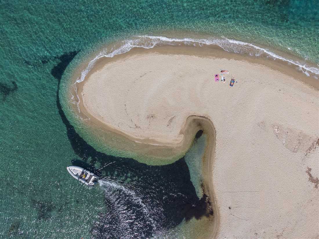 A boat passing the curved sand spit of Megali Ammos in turquoise water off Evia, the island coast an Evia day trip from Athens reaches.