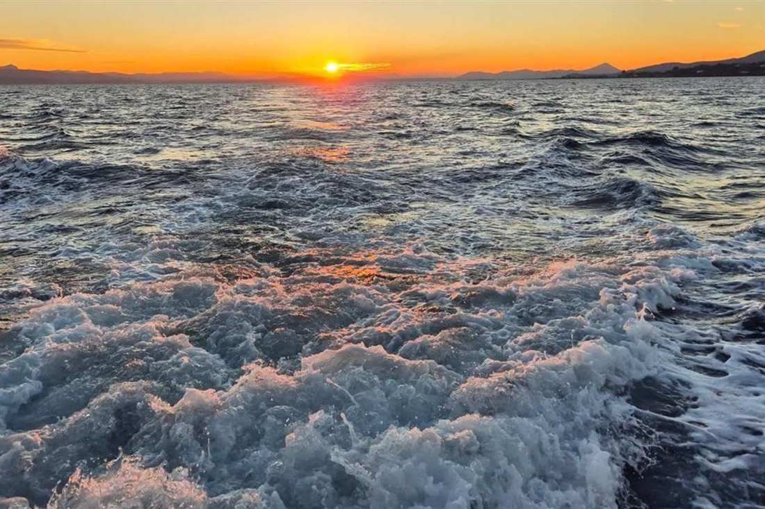 Orange sunset on the horizon over the Euboean Gulf, seen across the churning wake of a boat