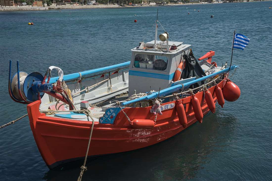 A red and white wooden fishing boat with a Greek flag moored in the harbour of Eretria on Evia