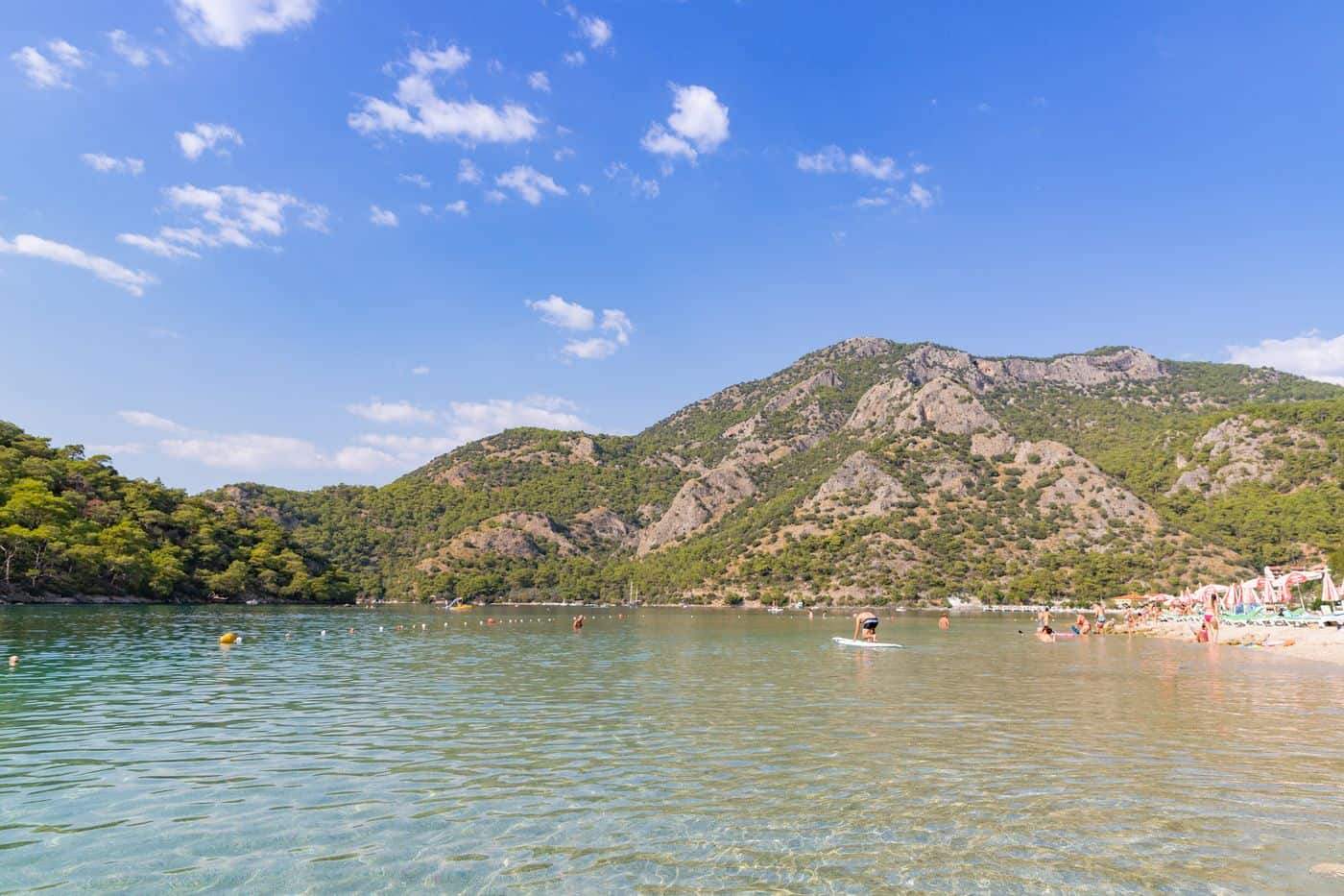 Fethiye tours reach the calm water of the Blue Lagoon at Oludeniz below the pine-covered hills