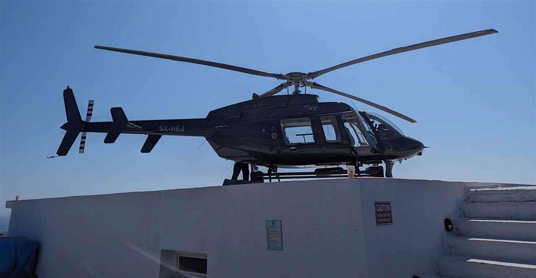 Black Bell 407 helicopter resting on a white rooftop helipad under a clear blue sky