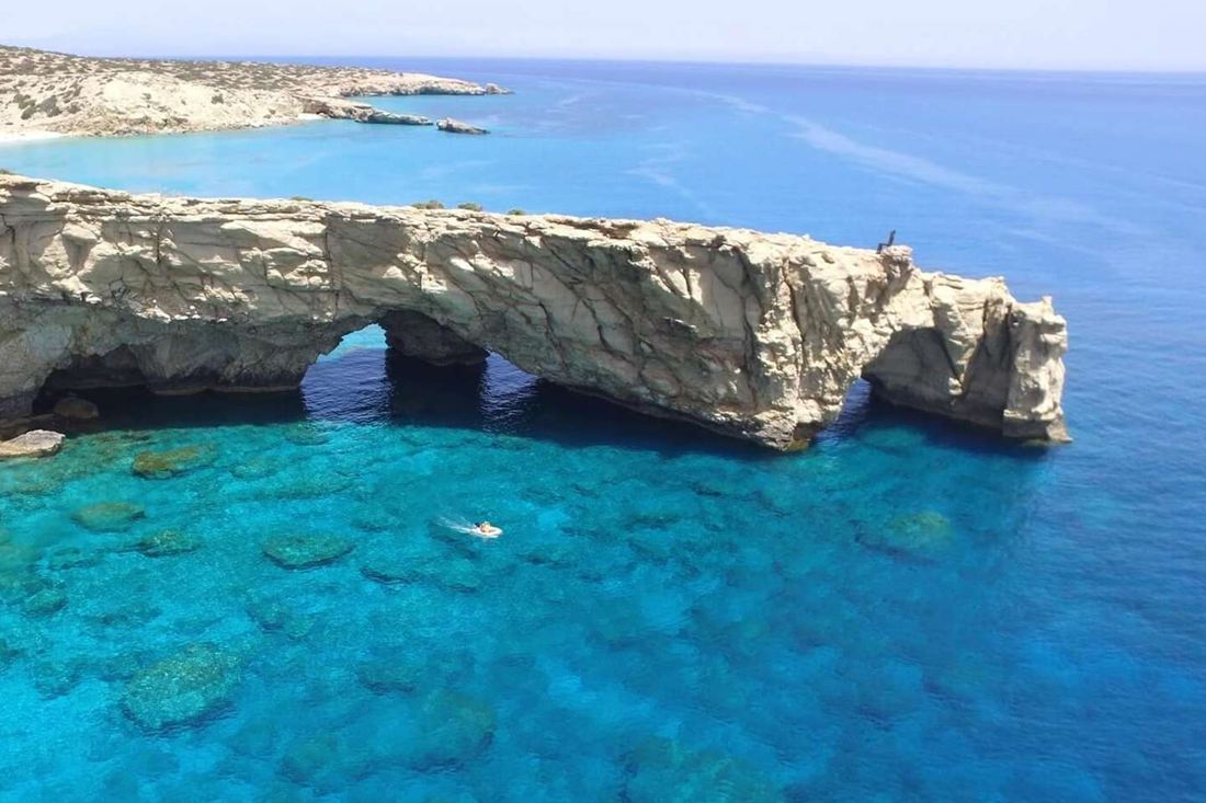 Turquoise water and a natural rock arch on the coast of Gavdos island with a small white boat leaving a wake