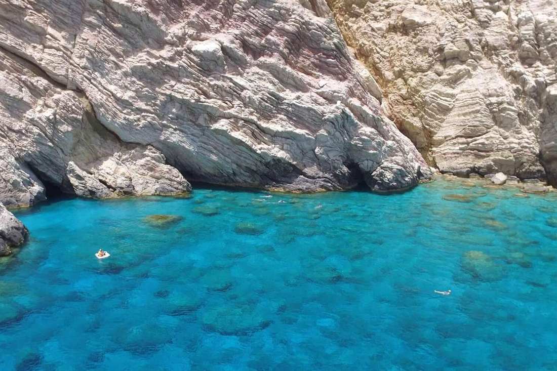 Clear turquoise cove below white limestone cliffs on Gavdos with swimmers in the water