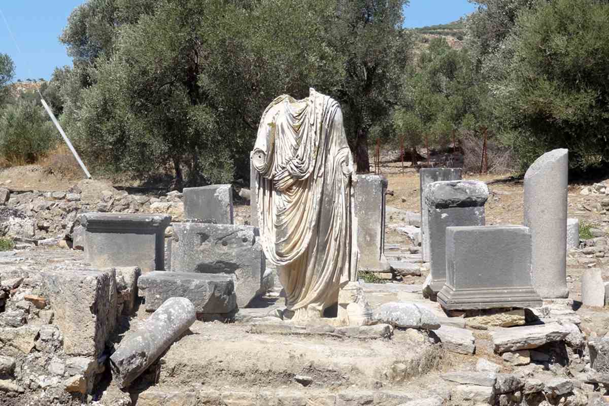 A headless Roman statue in a toga stands among olive trees at the Praetorium, the governor's seat in the Roman city that visitors buy Gortyna tickets to see.