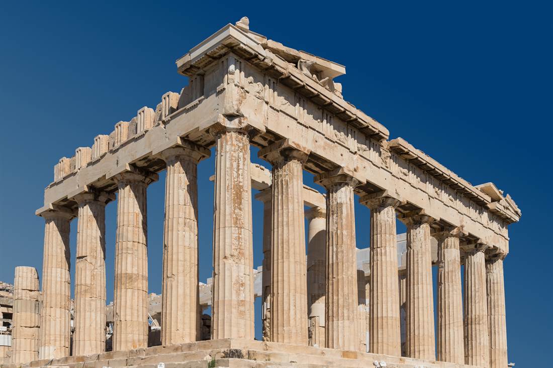 The Parthenon temple on the Acropolis in Athens, its columns and roof lit by sun against a deep blue sky