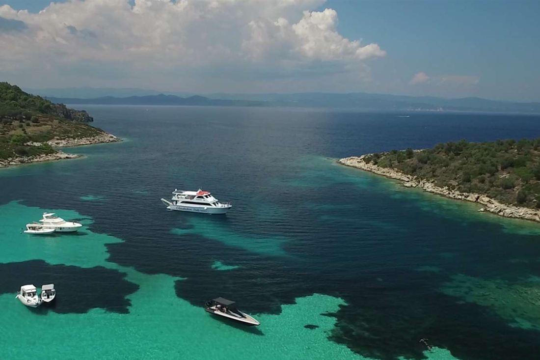 An aerial view of a turquoise Halkidiki bay with a tour boat and small boats between two green islands