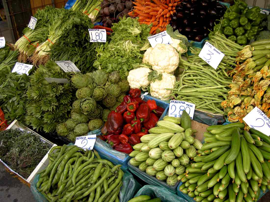 Artichokes, peppers, beans, courgette flowers and greens stacked on a vegetable stall in the Heraklion market, the colours of a Heraklion market tour.