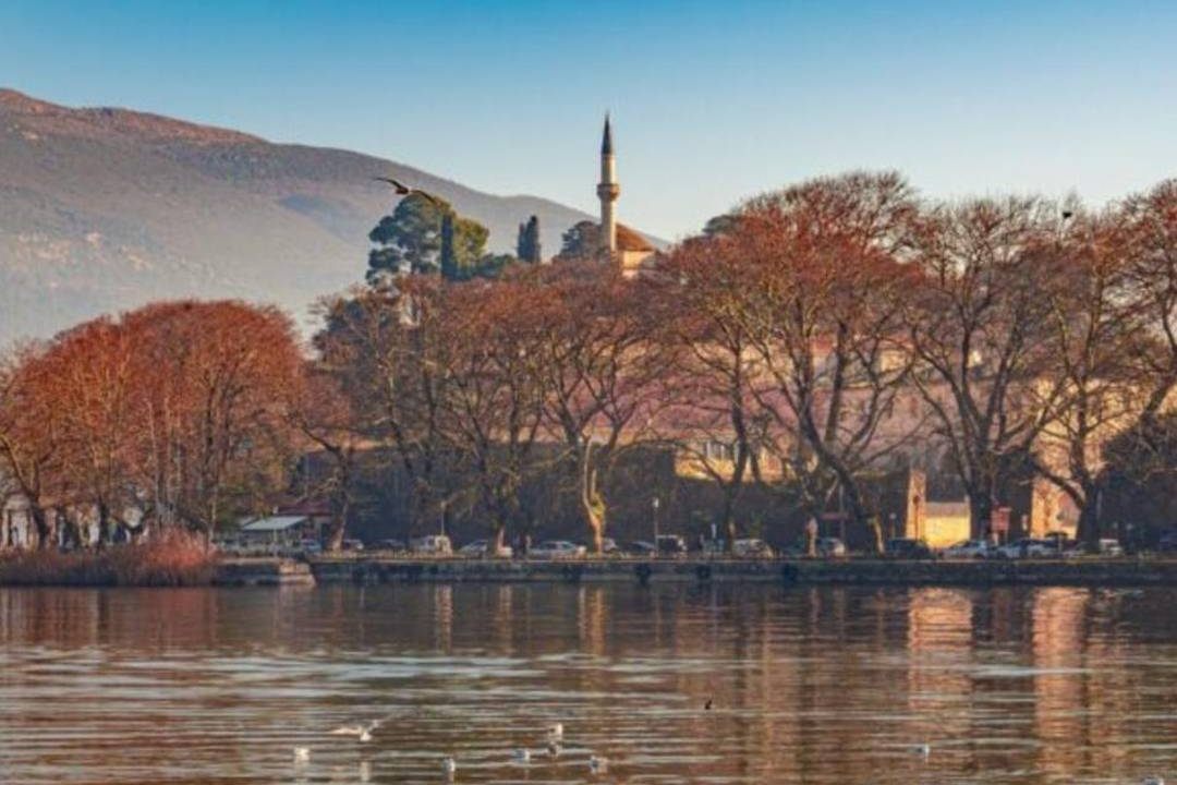 The minaret of the mosque on the castle of Ioannina above autumn trees, reflected in the still water of Lake Pamvotida.
