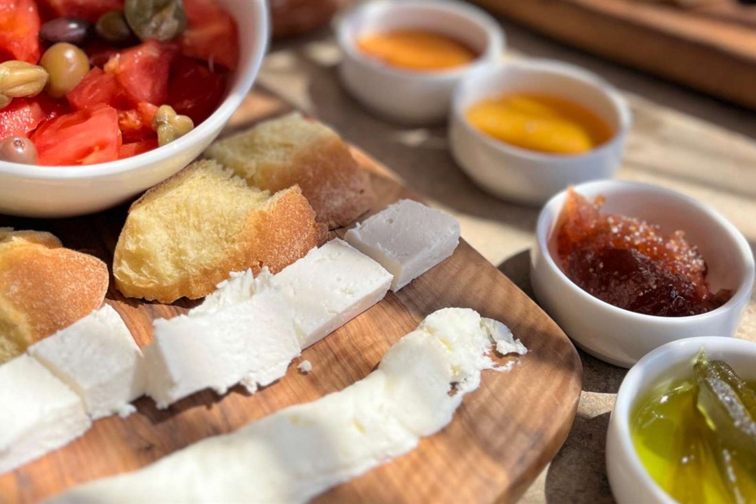 Local white cheeses, bread, tomato salad, honey and olive oil on a wooden tasting board