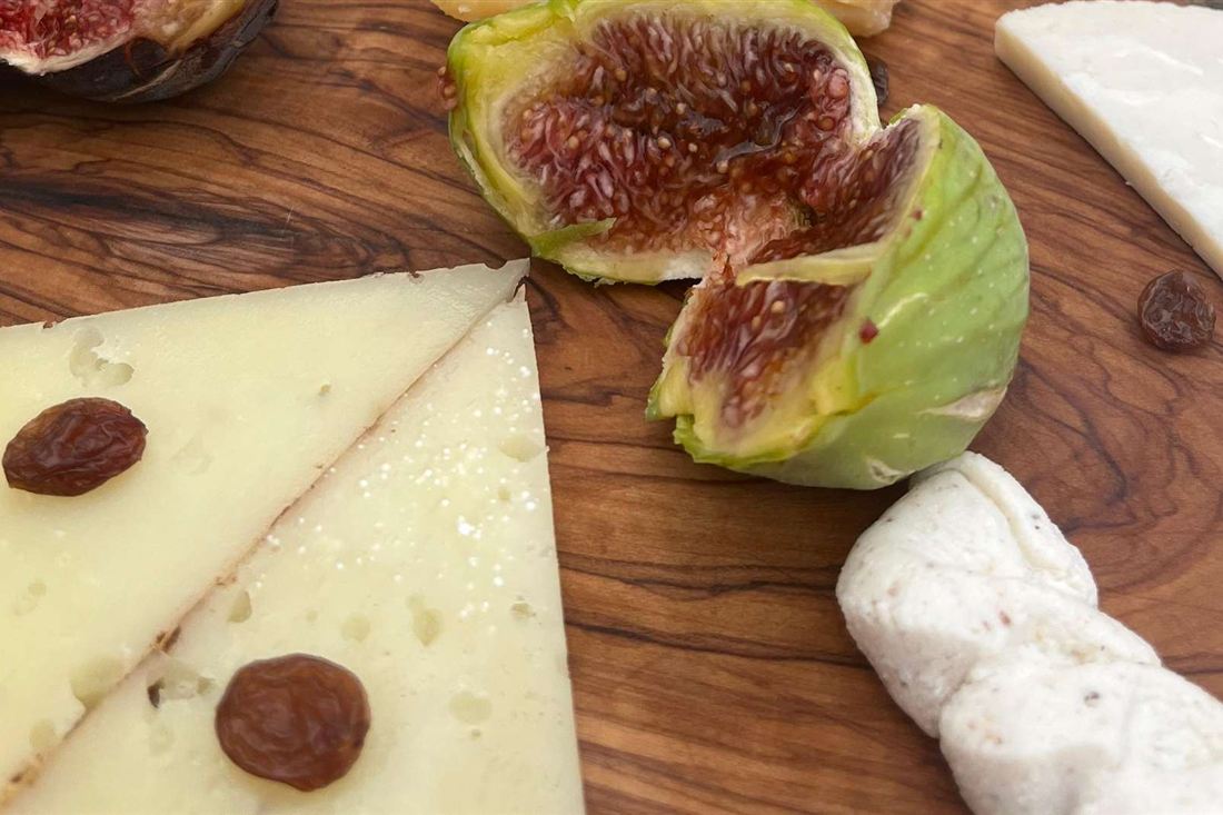 Slices of hard cheese with figs and raisins on an olive-wood board